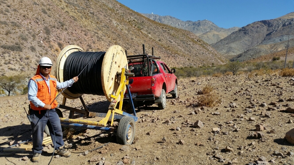 Again the backdrop of Cerro Pachón, a Telefonica/Cobra technician installs the AURA/LSST fiber optic cable from the AURA Gatehouse to the summit.  Telescopes on the summit, L-R, SOAR, Gemini-S, LSST.